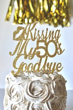 a white cake topped with a gold glitter happy birthday topper and the words kissing my 50 goodbye