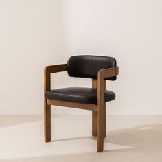 a wooden chair with black leather upholstered seat and back rests against a white wall