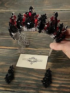 a hand holding a red and black tiara on top of a wooden table