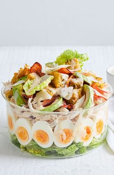 a salad with hard boiled eggs, bacon and lettuce in a glass bowl