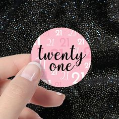 a hand holding a pink sticker with the words twenty one on it in black and white