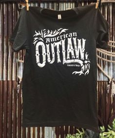 American Outlaw Country Western T shirt Who doesn't want to be an American Outlaw? This shirt screams country, western, and a complete bad a@#. This soft comfy T-shirt is available in vintage black. Fits Unisex Country Deep unisex T shirt 4.3 oz. 60% Cotton/40% Poly Black Letter Print Tops For Country Concerts, Black Short Sleeve Tops For Country Concerts, Black T-shirt With Letter Print For Country Concerts, Relaxed Fit Country Style Crew Neck T-shirt, Black Western Crew Neck Top, Black Graphic T-shirt For Country Concerts, Black Western Top With Graphic Print, Black Cotton Western T-shirt, Black Western Style Cotton T-shirt