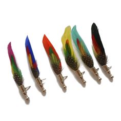 five different colored feathers are lined up in a row on a white surface with metal tips