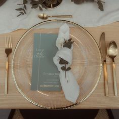 a place setting with napkins, silverware and gold cutlery on a wooden table