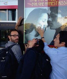 three people standing in front of a movie poster with one person reaching up to the sky