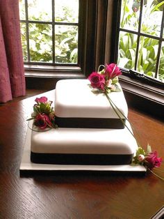 three tiered white cake with flowers on the top and bottom, sitting in front of a window