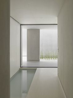 an empty hallway leading into a white room with glass doors on both sides and grass in the background