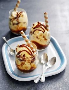 two desserts with ice cream and bananas on a plate next to spoons,