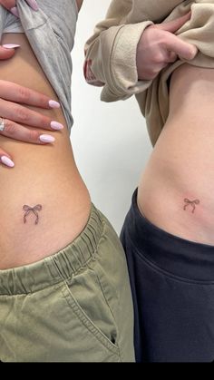 two women with tattoos on their stomachs and one is showing off her small bow tattoo