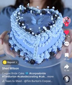 a woman holding a heart shaped cake with blue frosting and butterflies on it's top