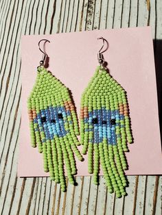 a pair of green and blue beaded earrings sitting on top of a wooden table