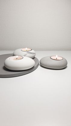 three lit candles sitting on top of each other in front of a white wall and floor