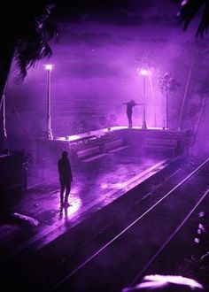 a person standing on a train track in the rain at night with purple light coming from behind