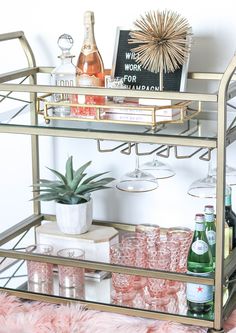 a bar cart filled with bottles and glasses on top of a pink furnishing