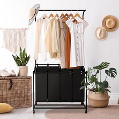 a rack with clothes hanging on it next to a basket and potted plant in the corner