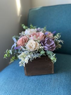 an arrangement of flowers in a wooden box on a blue chair with white and pink blooms