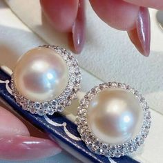 a pair of pearl and diamond earrings are displayed on a blue box with pink nail polish