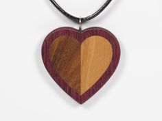 A wooden heart pendant made from afromosia (brown) and cherry (orange beige) inlaid in purpleheart (purple). The pendant is sanded smooth and finished with Danish Oil to bring out the grain of the wood and to add protection. The eyelet is made of stainless steel. The pendant is 1 5/8 Brown Heart Shaped Jewelry With Heart Beads, Heart-shaped Brown Necklace For Gift, Brown Heart-shaped Necklace For Gift, Brown Heart-shaped Necklace For Valentine's Day, Brown Heart Pendant Necklace For Valentine's Day, Brown Heart Necklace For Valentine's Day, Valentine's Day Heart-shaped Brown Necklace, Valentine's Day Brown Heart Necklace, Handmade Brown Heart Pendant Necklace