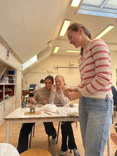 three women are sitting at a table working on something with one woman standing and looking down