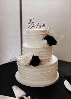 a white wedding cake with black and white flowers on the top is sitting on a table