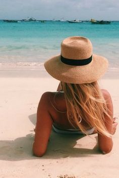 a woman in a hat is sitting on the beach