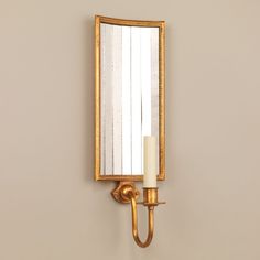 a candle is lit in front of a gold wall mounted mirror on a beige wall