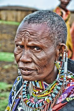 an old woman with many necklaces on her neck and face looking at the camera