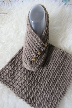 a knitted cowl with buttons on it sitting on top of a white rug