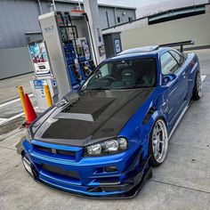 a blue car is parked in front of a gas station with its hood up and the engine on