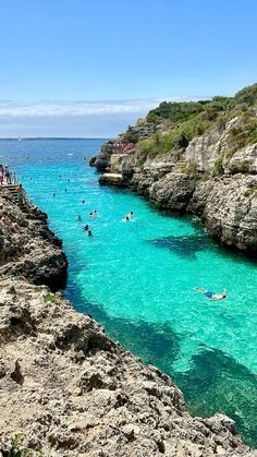 people are swimming in the blue water near some cliffs