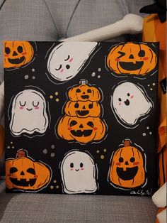 a black and orange halloween themed pillow with ghost faces on it's face, surrounded by pumpkins