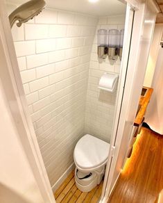 there is a toilet in the corner of this bathroom with wood flooring and white walls