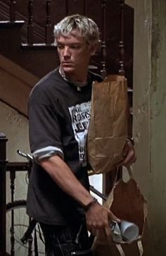 a man holding a brown paper bag next to a stair case