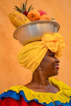 a woman wearing a yellow turban with fruit in it's bowl on her head