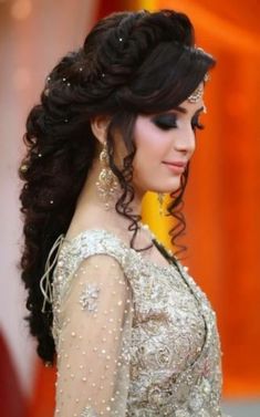 a woman with long hair wearing a white dress and gold jewelry on her head, standing in front of an orange curtain