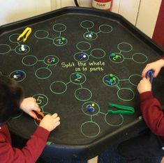 two young boys are sitting at a table with scissors and writing on the tray that says split the whole in to parts