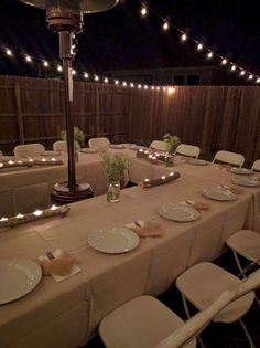 a long table set up with white plates and silverware for an outdoor dinner party