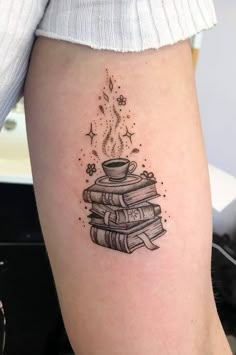 a woman's leg with a tattoo on it that has books and a cup