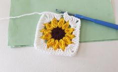 a crocheted square with a sunflower on it and a blue handled knitting needle