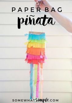 a person holding up a paper bag pinata hanging from the side of a house