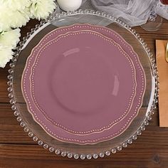 a pink plate sitting on top of a wooden table next to flowers and napkins