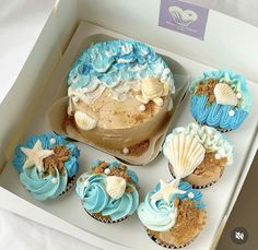 cupcakes with blue frosting and seashells in a box on a table