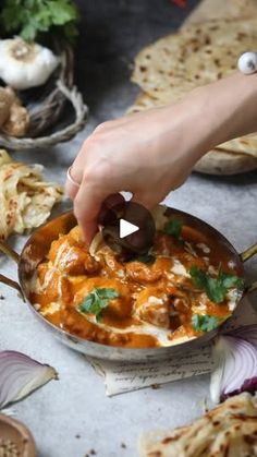 a person dipping an olive into a bowl of food with garlic and bread on the side