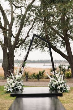 an outdoor ceremony setup with white flowers and greenery in front of some trees on the grass