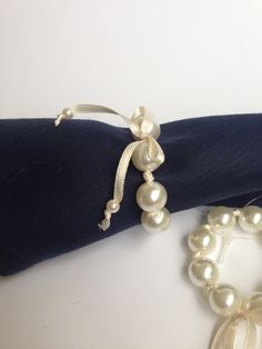 two bracelets on top of a blue napkin with white pearls and ribbon around it