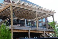 a large wooden deck with metal railings on the side of a house that's surrounded by greenery