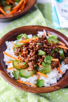 a wooden bowl filled with rice and meat on top of a green tablecloth covered table