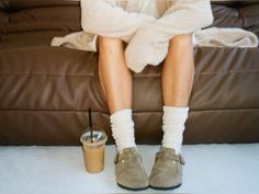 a woman sitting on top of a brown couch next to a coffee cup and blanket