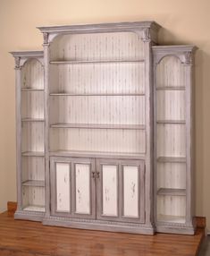 an old white bookcase with glass doors on the front and bottom shelves is sitting on top of a wooden floor