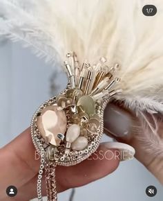 a person holding a brooch with pearls and feathers on it's back end